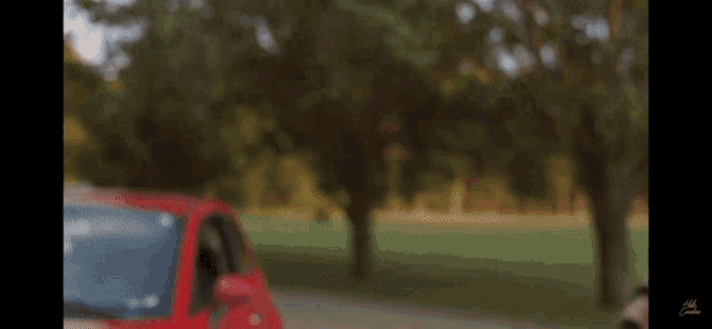 a red car is parked on the side of the road in front of trees