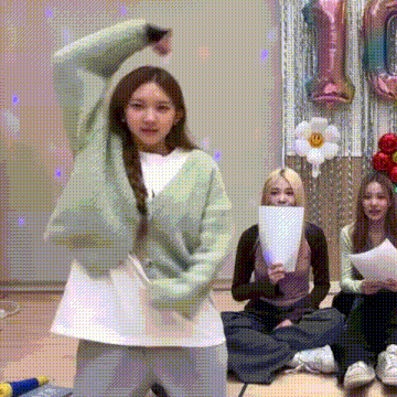 a girl in a green cardigan is dancing in front of a group of girls sitting on the floor .