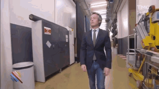 a man in a suit and tie is walking down a hallway with a sign on the wall that says no smoking