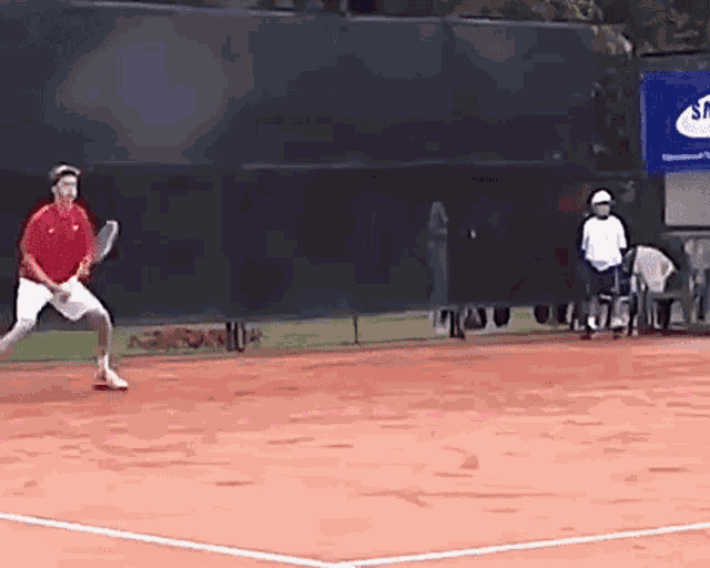 a man in a red shirt is playing tennis on a court in front of a samsung sign