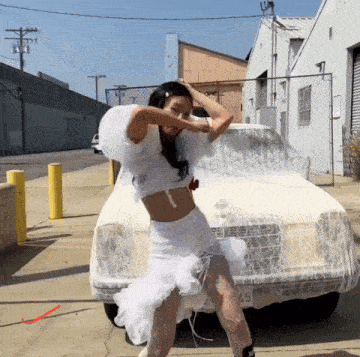 a woman in a white dress is dancing in front of a white car with a license plate that says 45
