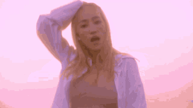 a woman is standing in front of a pink sky with her hand on her head
