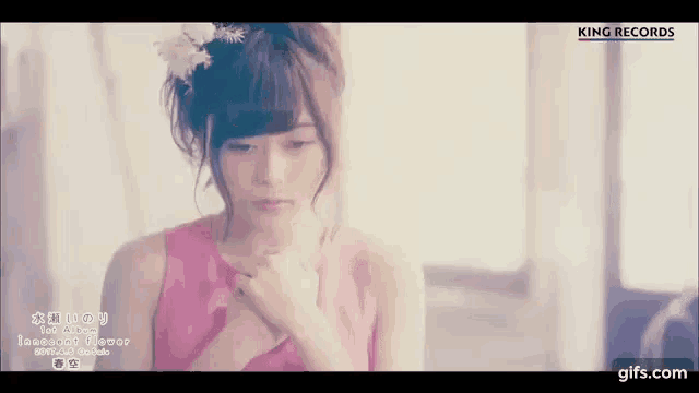 a woman in a pink dress with a flower in her hair is holding her chest .