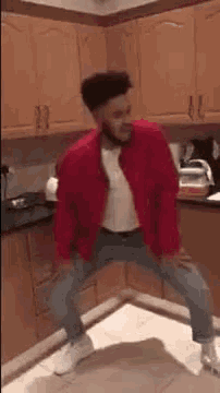 a man is dancing in a kitchen wearing a red jacket .