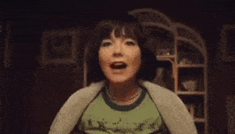 a woman in a green shirt is screaming with her mouth open in a dark room .