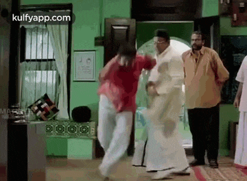a man in a red shirt is dancing in a living room with other men .