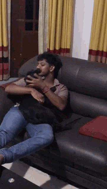 a man is sitting on a couch holding a small black dog