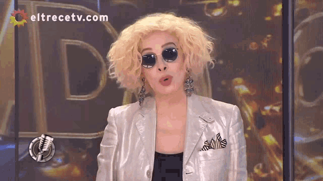 a woman wearing sunglasses and a silver jacket is on a television screen with eltrecetv.com in the upper right corner