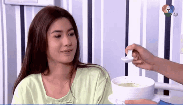 a woman in a hospital bed is being served a bowl of soup with a spoon