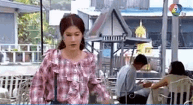 a woman in a pink plaid shirt is walking in front of a man sitting at a table .
