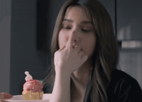 a woman is eating a cupcake with a strawberry frosting