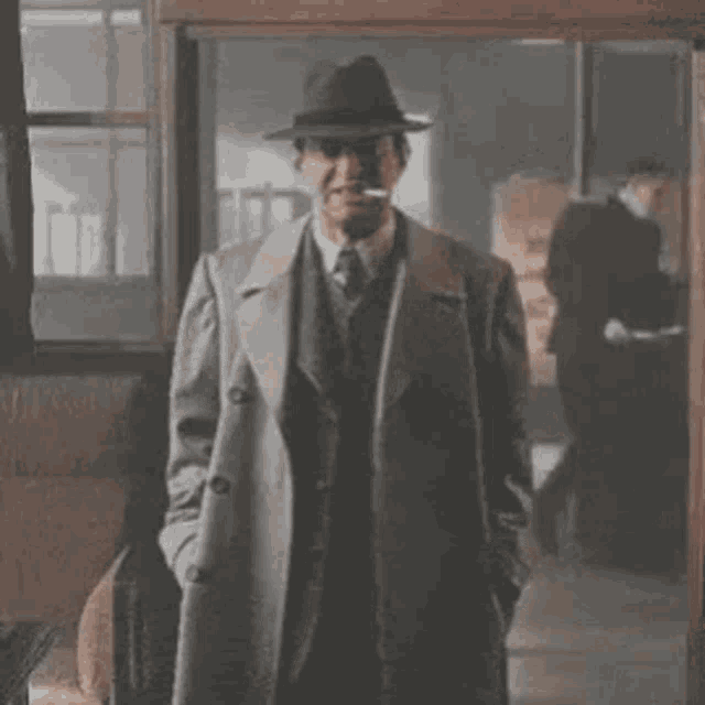 a man in a suit and hat is smoking a cigarette while standing in a doorway .