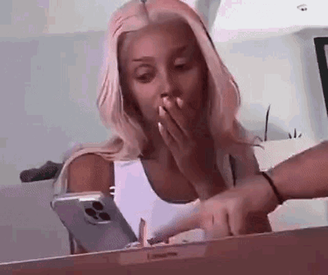 a woman with pink hair is sitting at a table with a laptop and a phone .