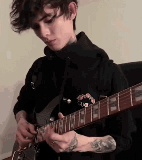 a man in a black hoodie is playing a guitar .