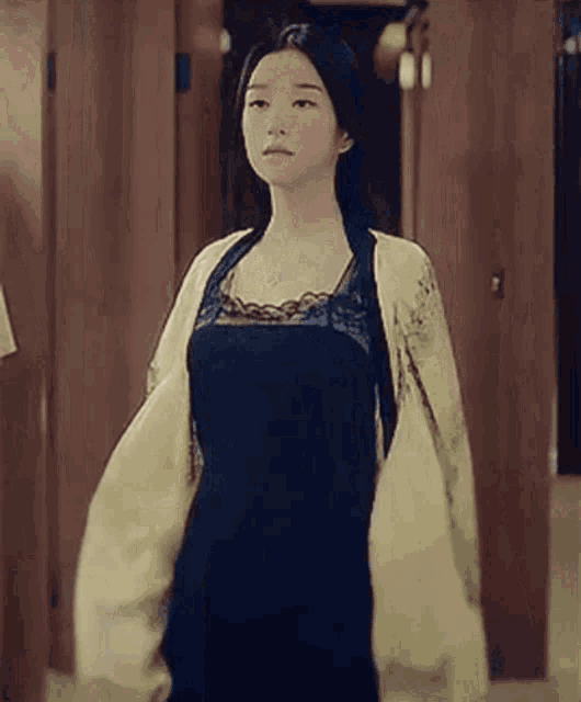 a woman in a black dress and a white jacket is standing in a dressing room .