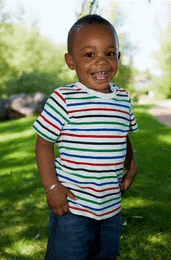 a young boy wearing a striped shirt and jeans is standing in the grass .