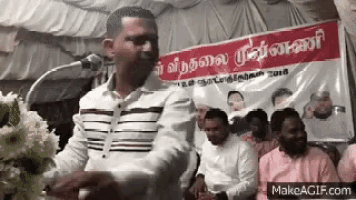 a man is giving a speech in front of a microphone while a group of people are sitting in front of him .