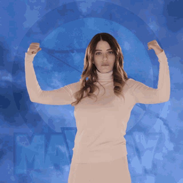 a woman in a white sweater flexes her muscles in front of a blue sky with the word may on it