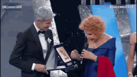 a man in a tuxedo is giving an award to a woman
