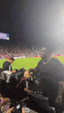 a man stands in the stands at a soccer game wearing a black shirt with the word adidas on it