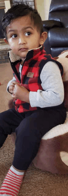 a young boy wearing a plaid vest and striped socks sits on a stuffed reindeer