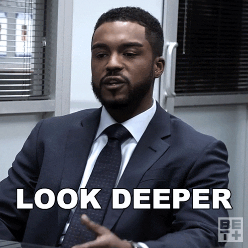 a man in a suit and tie is sitting at a table and says look deeper