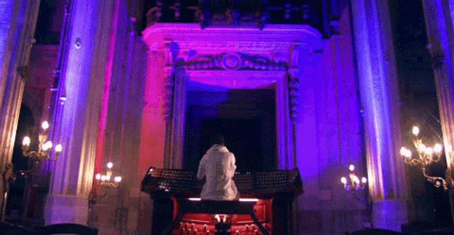 a man is playing an organ in a church with purple and pink lights behind him