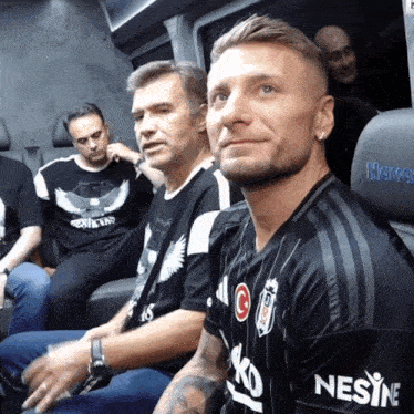 a man wearing a shirt that says nesine sits next to another man