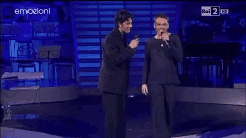 two men singing into microphones on a stage in front of a rai 2 hd screen