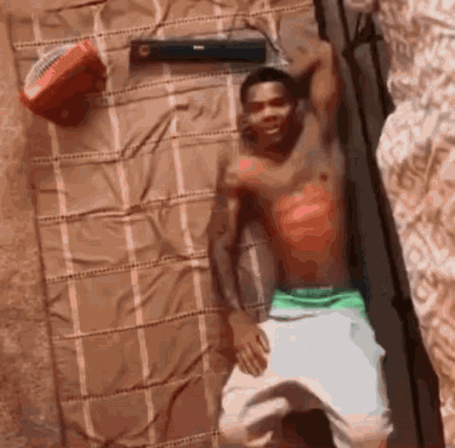 a shirtless man laying on a bed with a basketball on top of him