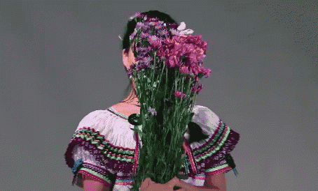 a woman wearing a traditional mexican dress is holding a bouquet of purple flowers .