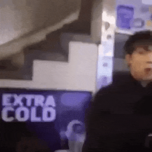 a man standing in front of a sign that says `` extra cold '' .
