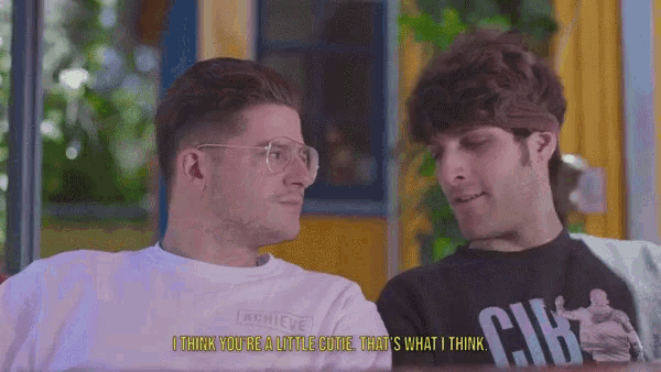 a man wearing a white shirt that says achieve talks to another man