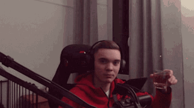 a man wearing headphones and a red hoodie is holding a glass in front of a microphone