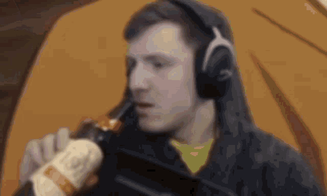 a man wearing headphones is drinking a bottle of beer .