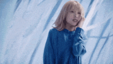 a woman in a blue shirt is standing in front of a blue wall