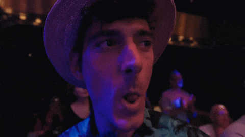 a man wearing a hat is making a funny face in a dark room