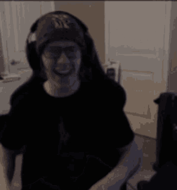 a man wearing headphones and a beanie is smiling while sitting in a dark room .