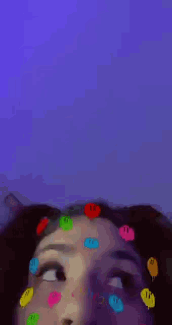 a girl with colorful smiley faces on her face is looking at the camera .