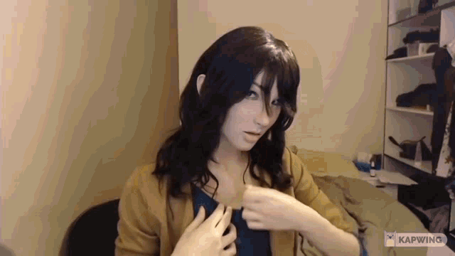 a woman is sitting at a desk in a room with her hands on her breasts .