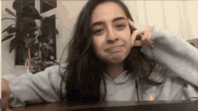 a woman in a grey sweatshirt is sitting at a table making a face