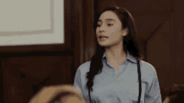 a woman in a blue shirt is standing in a room with a wooden wall .