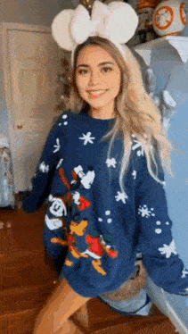 a woman wearing a mickey mouse headband and a blue sweater is standing in a room .