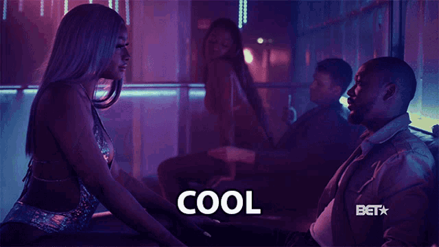 a man is sitting next to a woman in a club and the word cool is on the screen