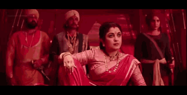 a woman in a red saree is sitting in front of a group of men in red clothes .