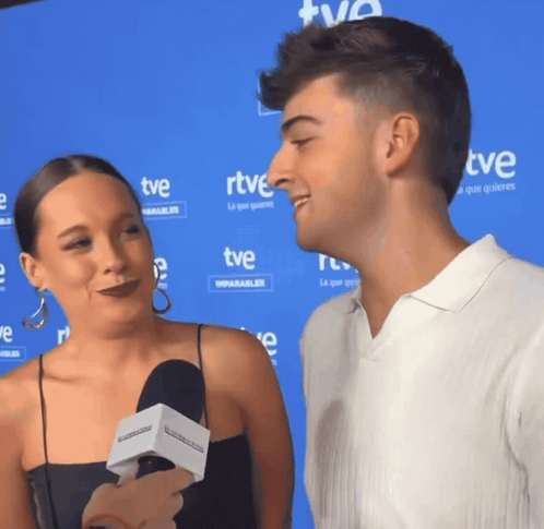 a man and a woman are talking in front of a blue wall with rtve written on it