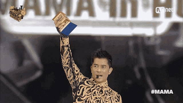a man holds up a trophy in front of a mnet sign