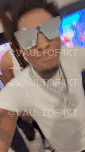 a man wearing sunglasses and a white shirt with the words vaultof4kt on the bottom right