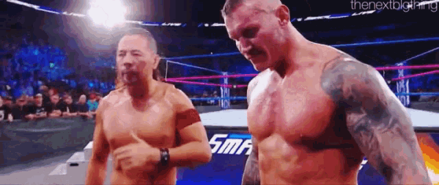 two men are standing next to each other in a wrestling ring and one of them is giving the other a thumbs up .