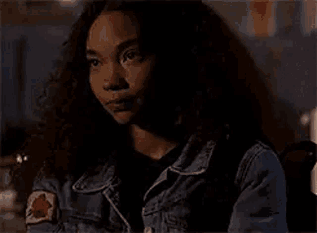 a woman with curly hair is wearing a denim jacket and backpack .